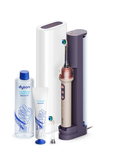 Набір продуктів Dyson: світло-рожева щітка в док-станції, футляр, насадка, білий тюбик зубної пасти та пом'якшувач тканини