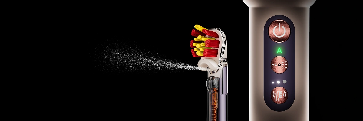 Końcówka Dyson Sensitive z czerwono-żółtym włosiem z dyszą irygatora. Obok zbliżenie na korpus szczoteczki Dyson i przyciski