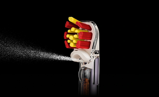 Zbliżenie na końcówkę Dyson Sensitive z czerwono-żółtym włosiem oraz dyszę irygatora, z której wydobywa się woda