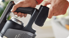 Osoba trzyma akumulator i odkurzacz z widocznym napisem \'PHILIPS AquaTrio Series 9000\'.