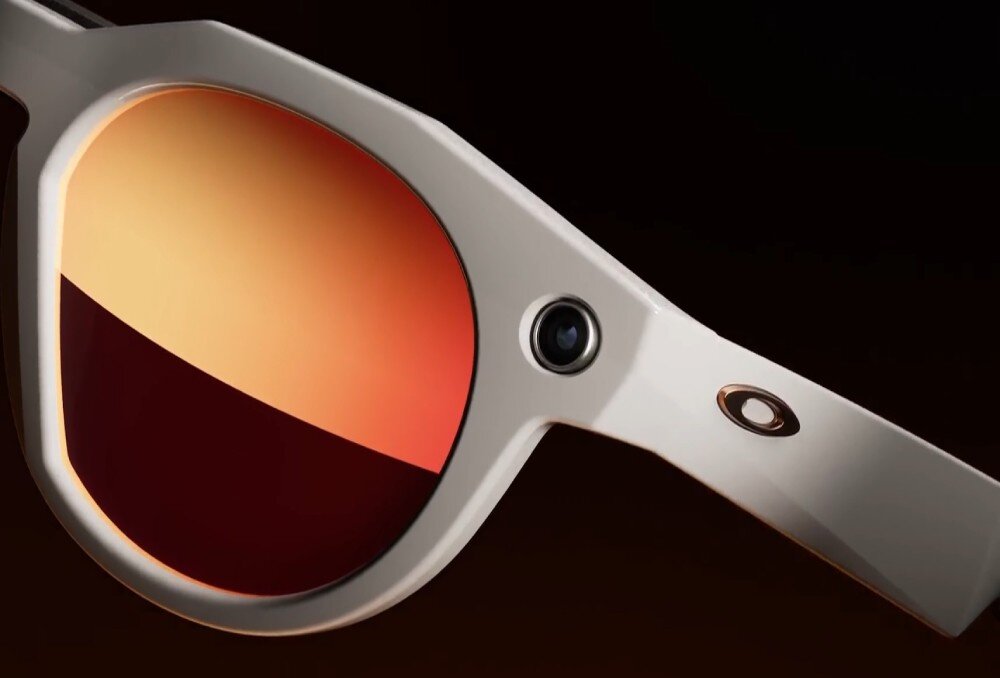 Okulary z przezroczystymi oprawkami i soczewkami w odcieniach pomarańczowego, z widocznym logo Oakley na zauszniku.