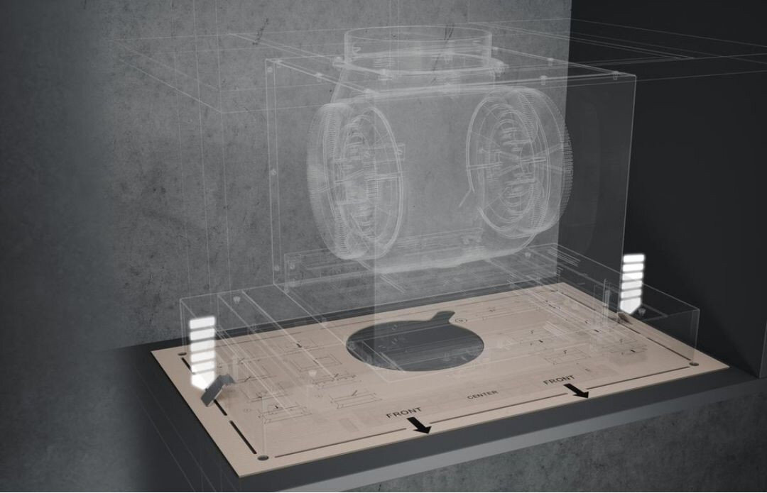 Obraz przedstawia przezroczysty model okapu z widocznymi elementami wewnętrznymi, umieszczony na powierzchni z oznaczeniami \'FRONT\' i strzałkami wskazującymi kierunek. Tło jest szare i jednolite.