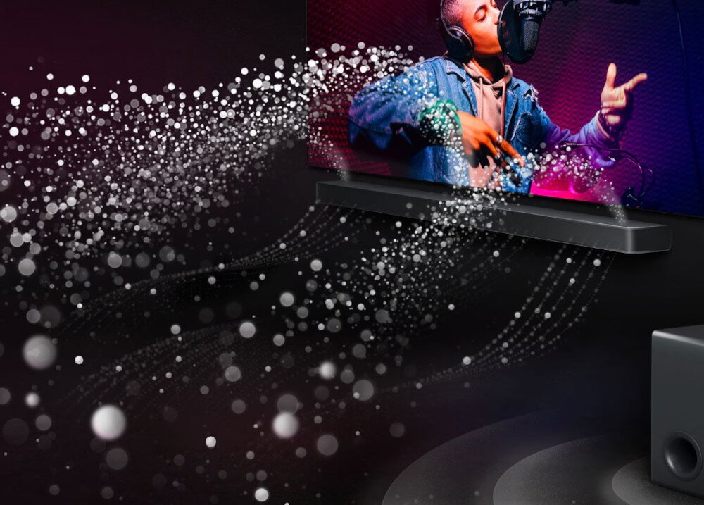 Obraz przedstawia soundbar umieszczony pod telewizorem, na którym widoczna jest osoba śpiewająca do mikrofonu. Wokół soundbara i subwoofera unoszą się efekty wizualne przypominające fale dźwiękowe.