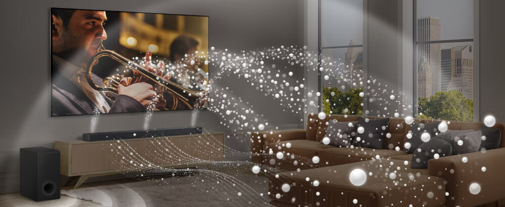 W salonie znajduje się duży telewizor z obrazem muzyka grającego na trąbce, a przed nim ustawiony jest soundbar i subwoofer. Wokół rozchodzą się wizualizacje dźwięku w postaci białych, świetlistych kul i linii.