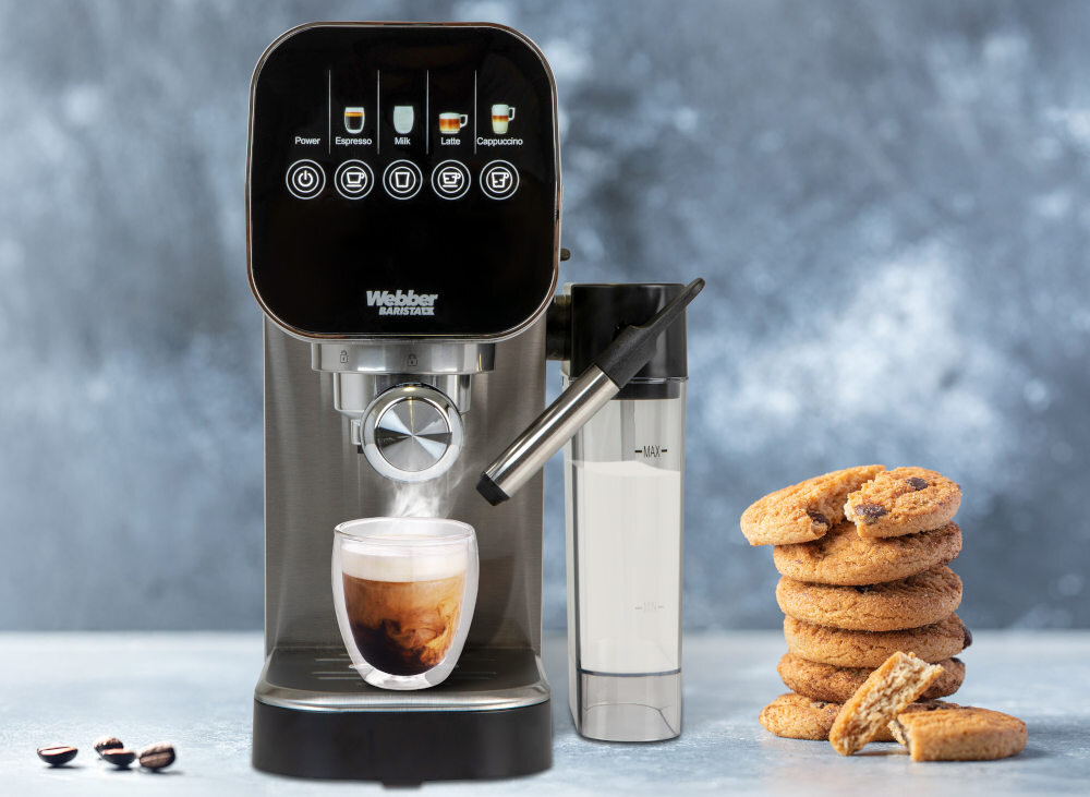 Na obrazie znajduje się ekspres do kawy z logo \'Webber BARISTA H5\', obok którego stoi pojemnik na mleko. Przed ekspresem znajduje się filiżanka z kawą, a obok leży stos ciastek.