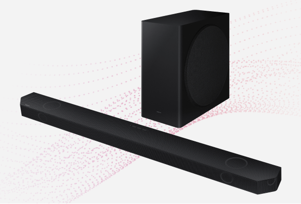 Na obrazie widoczny jest czarny soundbar oraz bezprzewodowy subwoofer. Tło jest jasne z delikatnym wzorem w postaci różowych kropek.