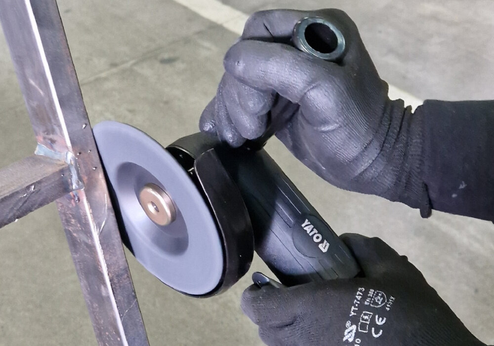 Szlifierka kątowa YATO YT-09675 osoba używa szlifierki zbliżenie na tarczę współpraca z tarczą o średnicy 125 mm z otworem 16 lub 22 mm gwint wrzeciona M10 szybkie i stabilne mocowanie tarcz kluczyk w zestawie płynność pracy