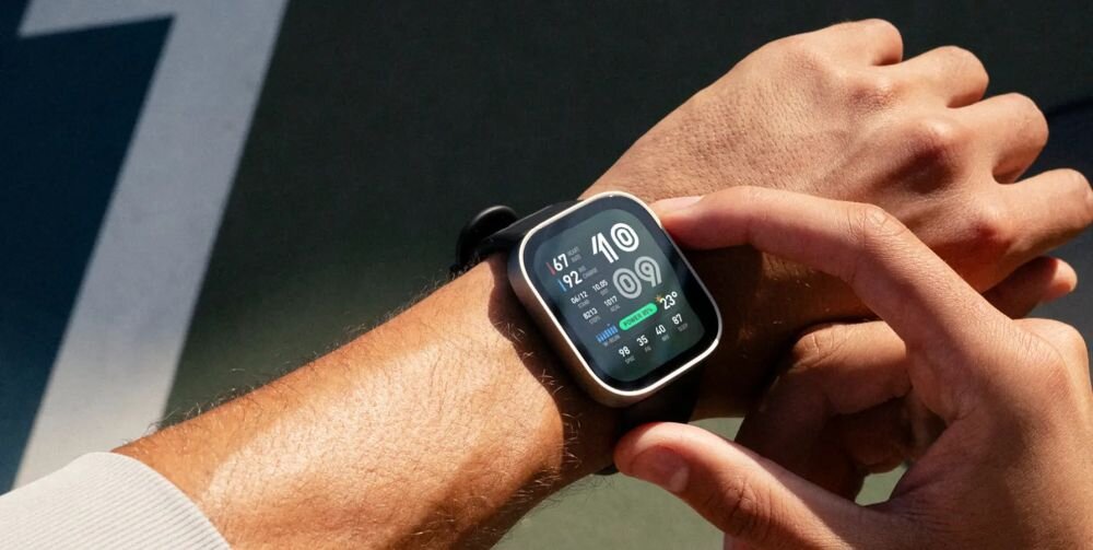 Osoba nosi smartwatch z wyświetlaczem pokazującym dane takie jak kroki, kalorie i pogodę. Zegarek ma ciemnoniebieski pasek.