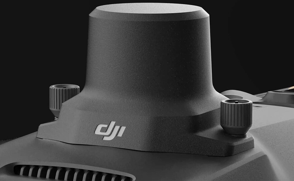 Zbliżenie na górną część drona z widocznym logo \'DJI\'. Obudowa jest w kolorze ciemnoszarym z dwoma pokrętłami po bokach.