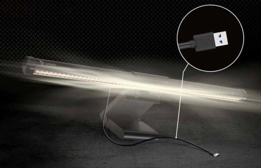 Lampka na monitor z logo \'SAVIO\' emituje jasne światło, z widocznym kablem USB do zasilania. W tle ciemne tło z teksturą, a w powiększeniu pokazano końcówkę USB.
