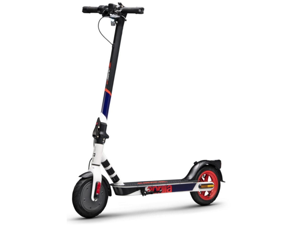 Hulajnoga elektryczna w kolorach biało-czarno-czerwonym z widocznym logo \'aprilia\' na podeście. Posiada czerwone koła i czarną kierownicę z elementami białymi i niebieskimi.