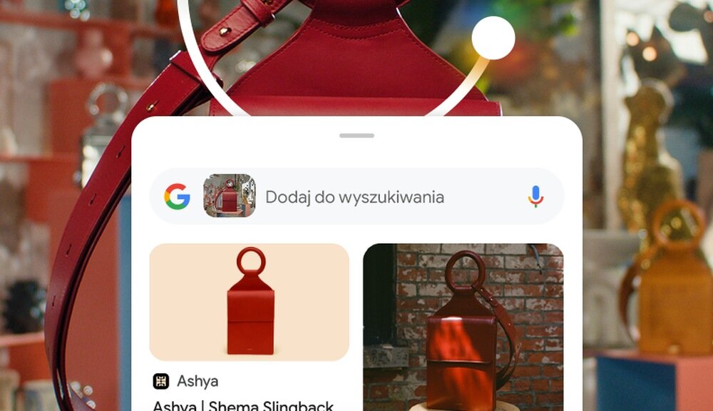 Na obrazie widoczny jest ekran smartfona z aplikacją wyszukiwania, na którym znajduje się zdjęcie czerwonej torby z okrągłym uchwytem. W tle widać rozmyte elementy dekoracyjne i inne torby.
