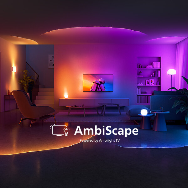 Pokój oświetlony kolorowymi światłami, z telewizorem na ścianie i nowoczesnymi meblami. Na obrazie widoczny jest tekst: \'AmbiScape Powered by Ambilight TV\'.
