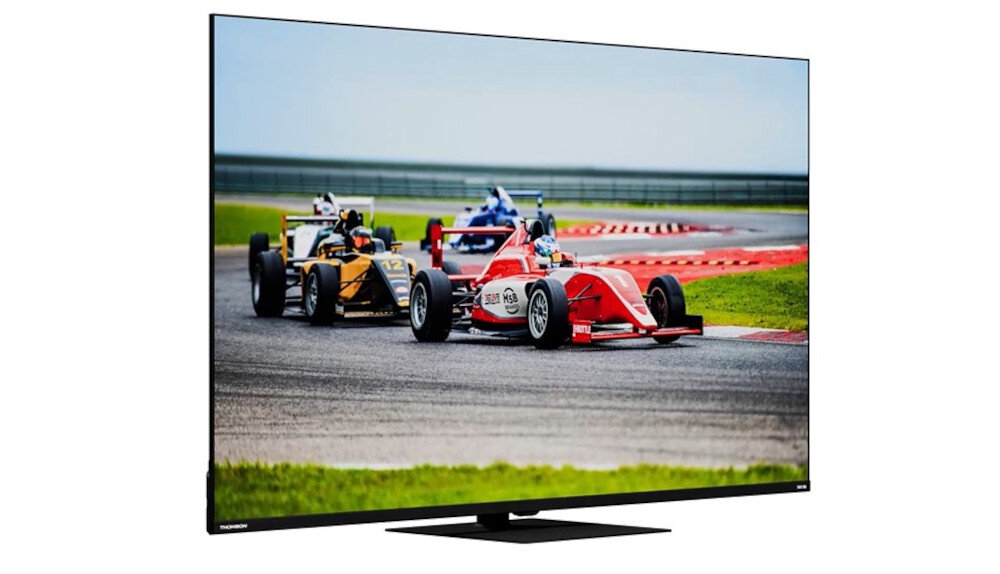 Telewizor wyświetla obraz wyścigu samochodowego na torze, z kilkoma pojazdami w ruchu. Na dolnej ramce widoczne jest logo \'THOMSON\'.