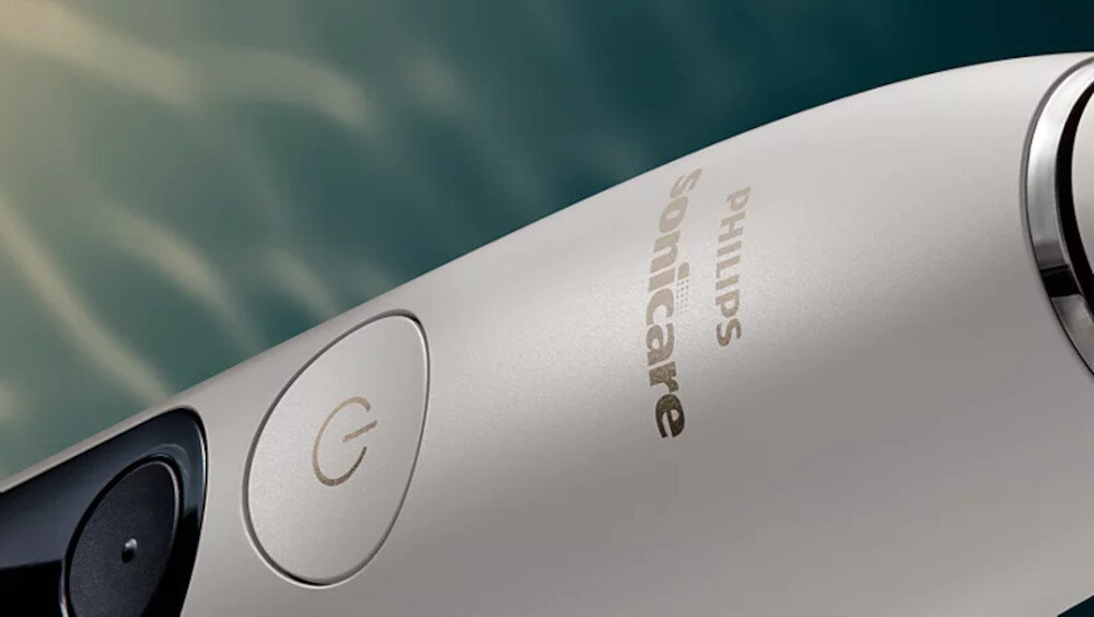 Zbliżenie na białą szczoteczkę soniczną z widocznym przyciskiem zasilania i logo \'PHILIPS Sonicare\'.