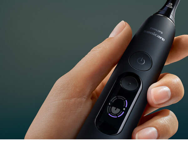 Osoba trzyma czarną szczoteczkę soniczną z widocznym logo \'philips sonicare\' oraz przyciskiem zasilania. Na szczoteczce znajduje się również wskaźnik z literami \'L\' i \'R\'.