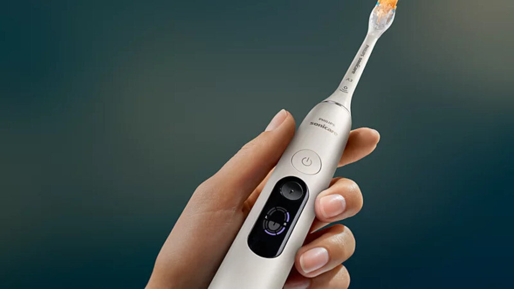 Osoba trzyma białą szczoteczkę soniczną z widocznym przyciskiem zasilania i logo \'Philips Sonicare\'.