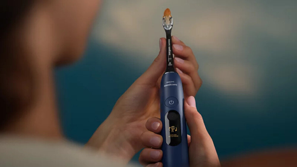 Osoba trzyma granatową szczoteczkę soniczną z widocznym przyciskiem zasilania i napisem \'Sonicare\'.