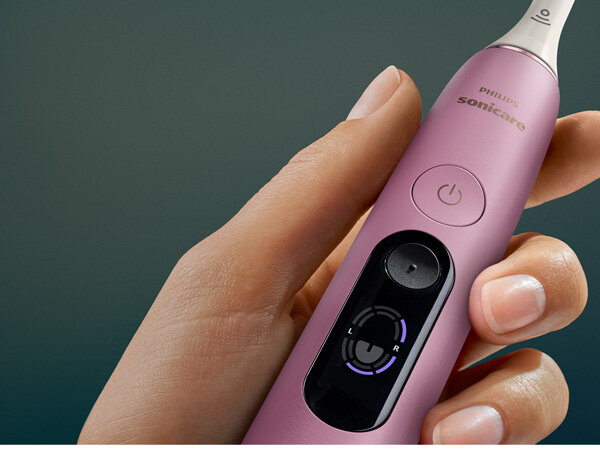 Różowa szczoteczka soniczna trzymana w dłoni, z widocznym przyciskiem zasilania i logo \'PHILIPS Sonicare\'.