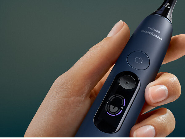 Osoba trzyma granatową szczoteczkę soniczną z widocznym logo \'PHILIPS sonicare\' oraz przyciskiem zasilania. Na wyświetlaczu widoczne są oznaczenia \'L\' i \'R\'.