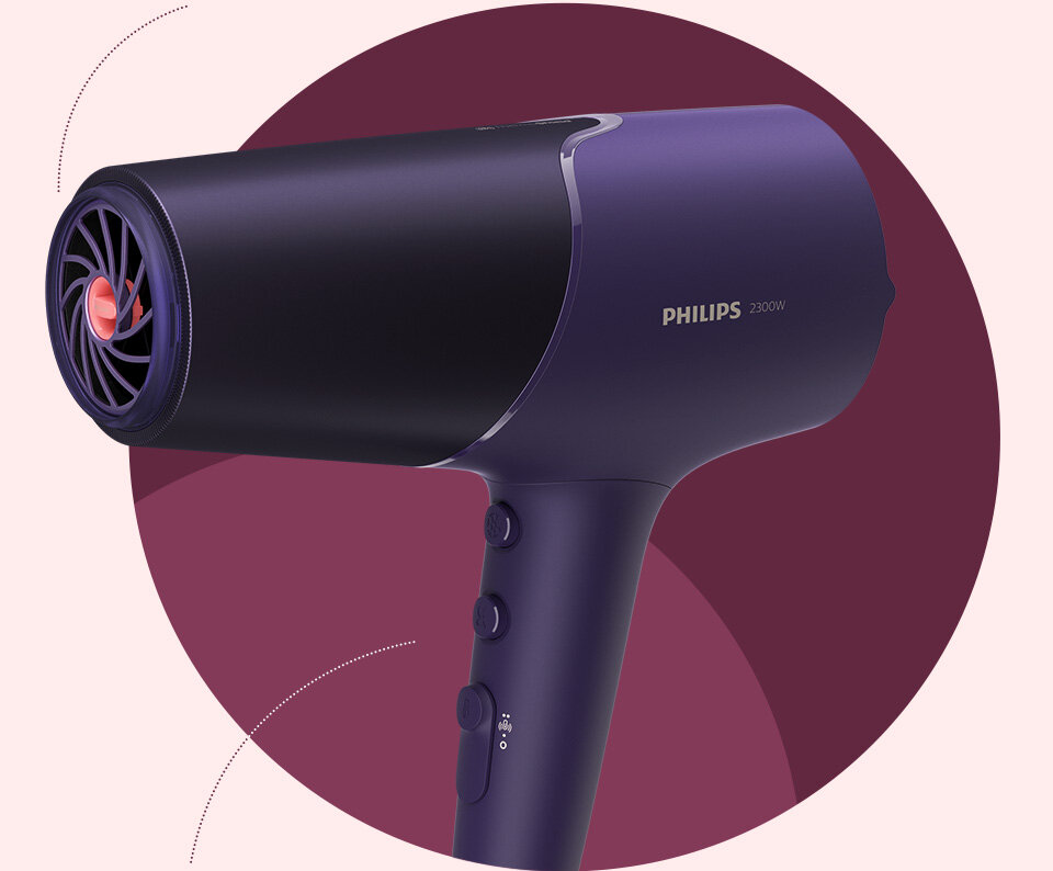 Na obrazie widoczna jest suszarka do włosów w kolorze fioletowym z logo \'PHILIPS 2300W\'. Suszarka ma kilka przycisków na uchwycie i widoczny jest wylot powietrza z czerwonym elementem w środku.