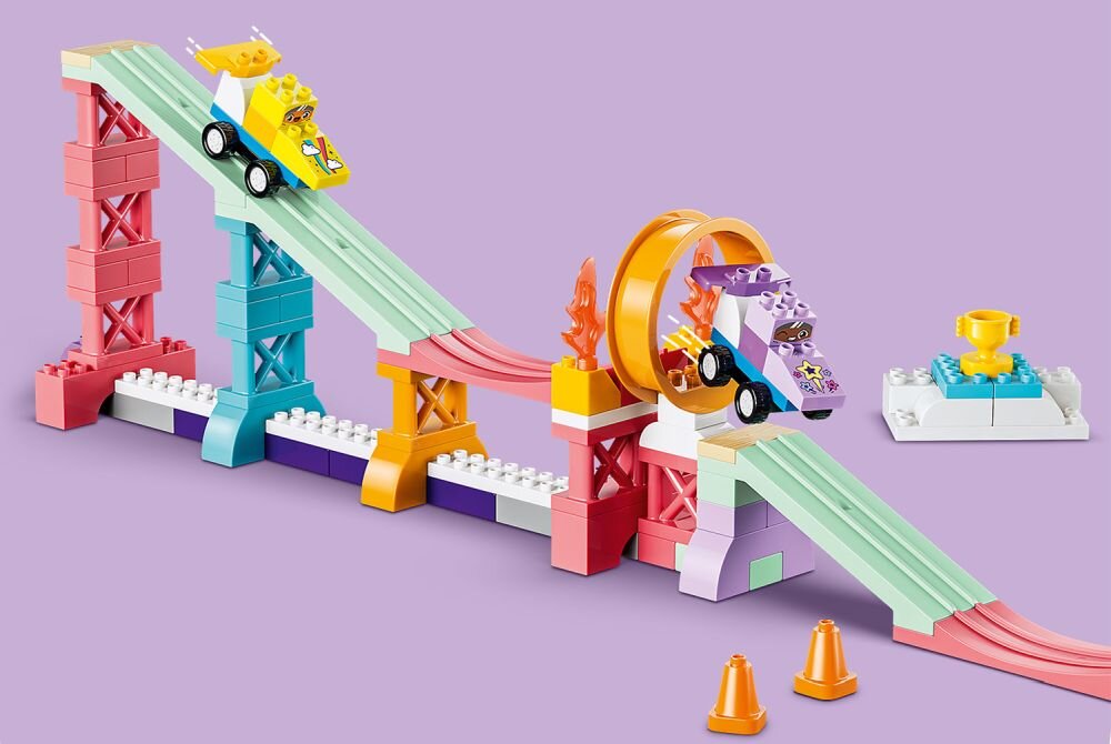 Zestaw LEGO składający się z kolorowych ramp, pojazdów i pętli, zbudowany na fioletowym tle. Obok rampy znajdują się dwa pomarańczowe pachołki i mała platforma z żółtym pucharem.