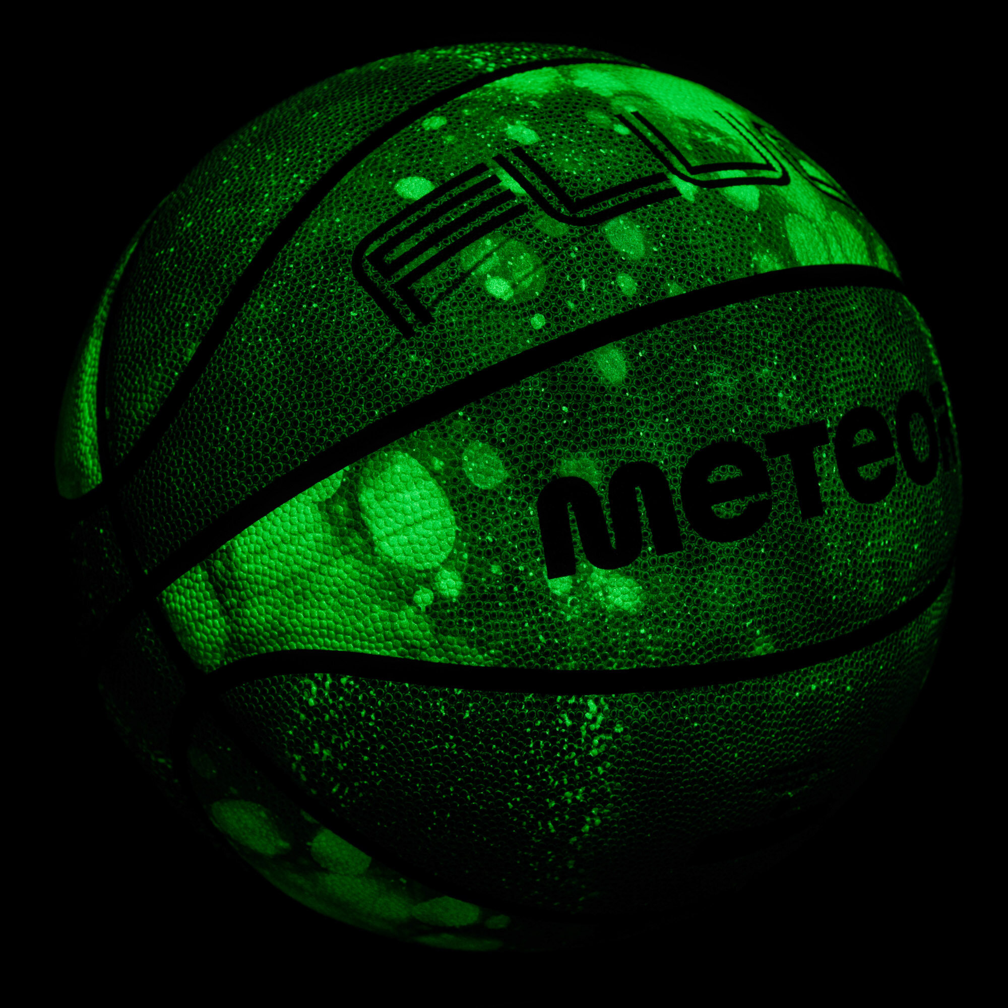 Piłka do koszykówki z widocznymi napisami \'FLUO\' i \'meteor\', świecąca w ciemności na zielono z białymi plamkami.