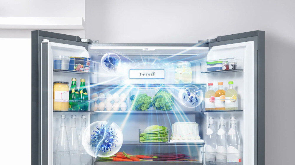 Otwarta lodówka z widocznymi produktami spożywczymi, takimi jak jajka, warzywa, napoje i słoiki. Na środku widoczny jest napis \'T-Fresh\' oraz efekty świetlne sugerujące chłodzenie.