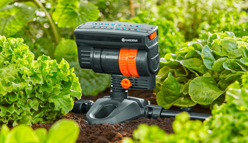 Zraszacz GARDENA Micro-Drip-System 13325-20 umieszczony w ogrodzie wśród zielonych roślin. Na urządzeniu widoczne jest logo \'GARDENA\'.