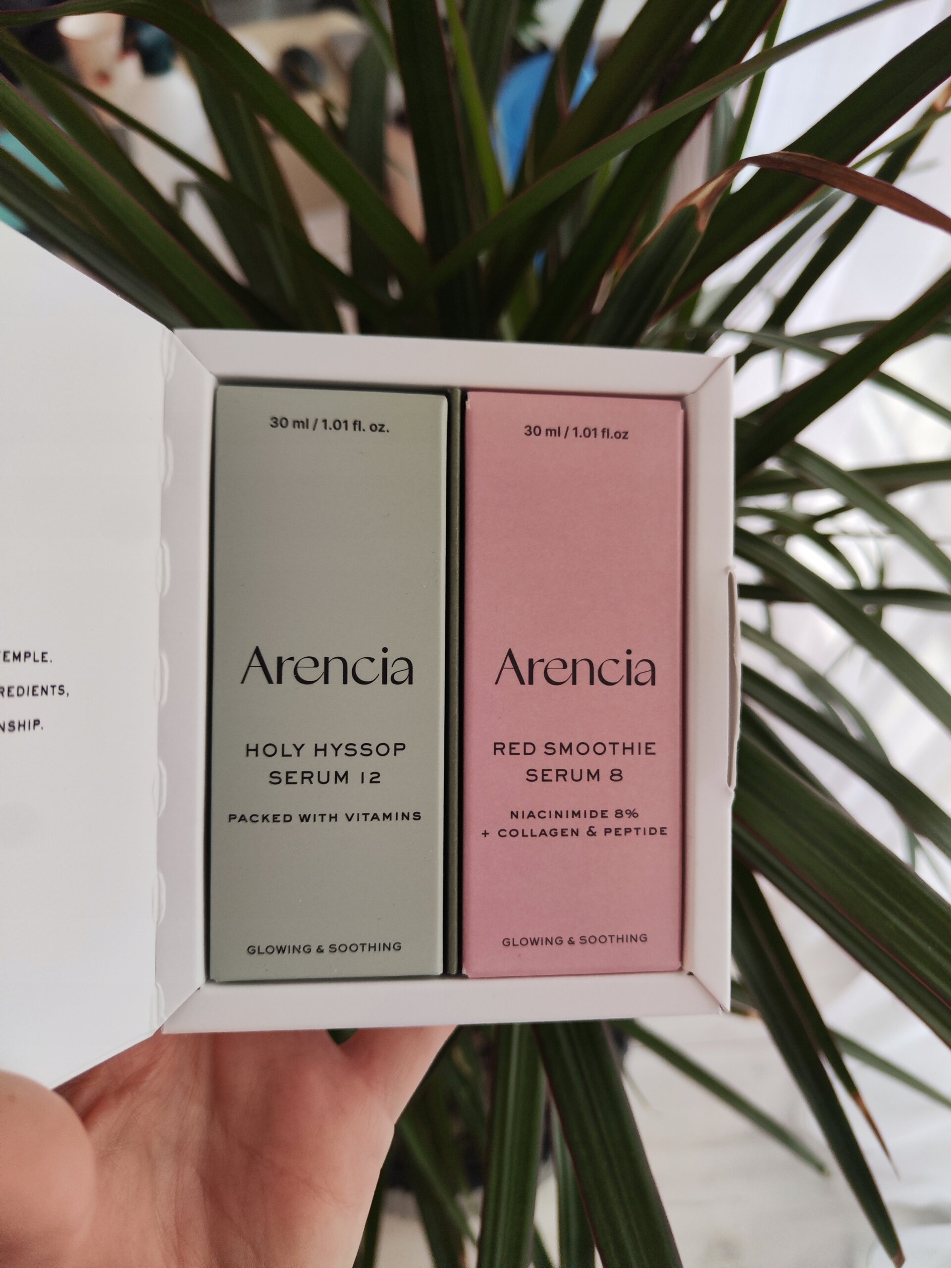 Zdjęcie przedstawia otwarte pudełko z dwoma buteleczkami serum marki Arencia. Na opakowaniach widnieją napisy: \'HOLY HYSSOP SERUM 12\' oraz \'RED SMOOTHIE SERUM 8\'.