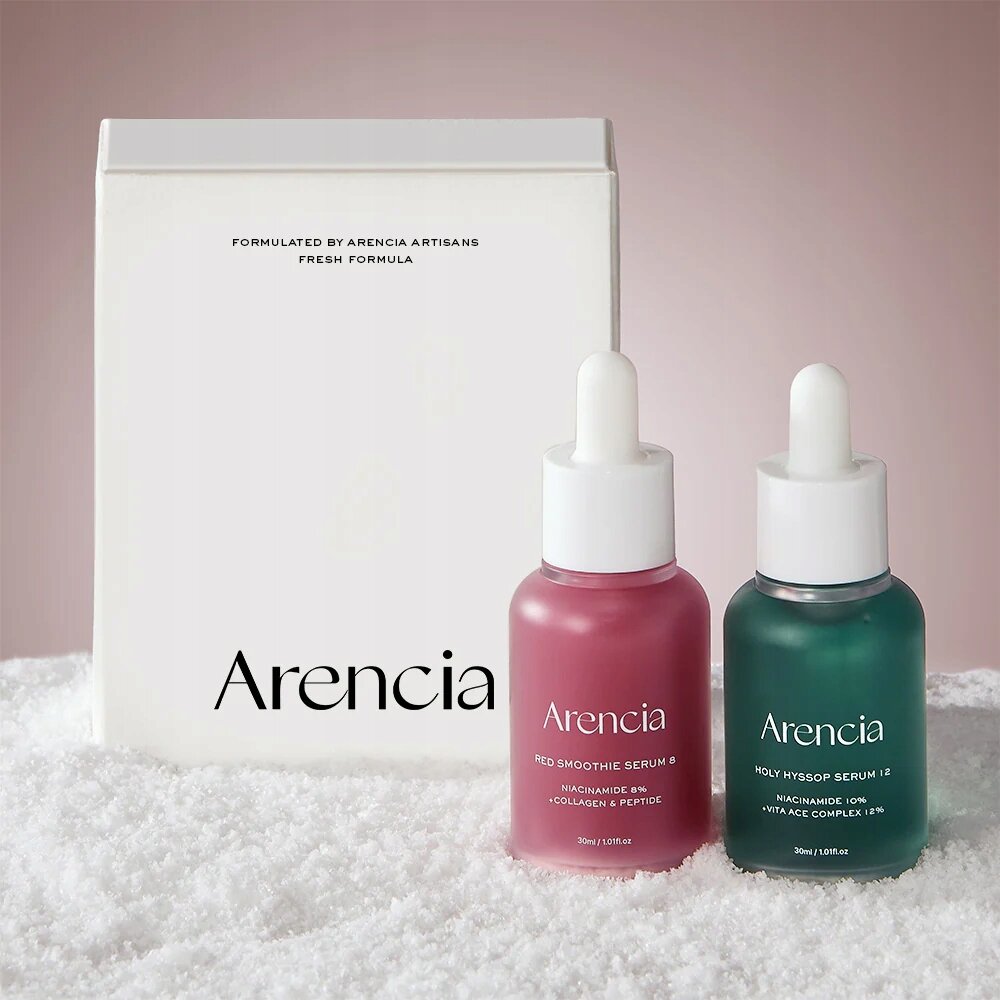 Na obrazie znajdują się dwa kolorowe flakony serum do twarzy z pipetami, jeden różowy z napisem \'Arencia Red Smoothie Serum 8\' i drugi zielony z napisem \'Arencia Holy Hyssop Serum 12\'. W tle widoczny jest biały kartonik z napisem \'FORMULATED BY ARENCIA ARTISANS FRESH FORMULA\'.