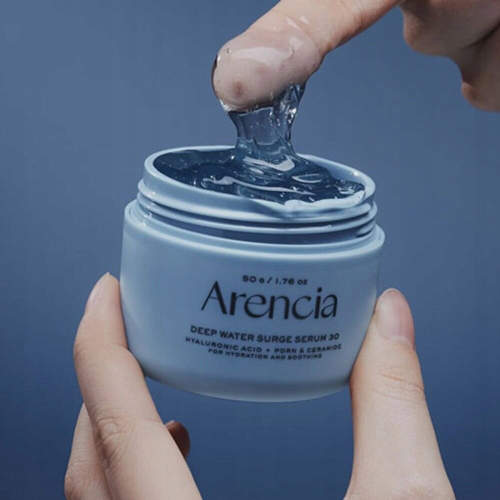 Osoba trzyma otwarty słoik z niebieskim żelem, na którym widnieje napis: \'Arencia DEEP WATER SURGE SERUM 30 HYALURONIC ACID + PDRN & CERAMIDE FOR HYDRATION AND SOOTHING\'.