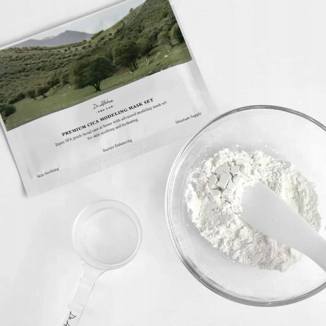 Na obrazie widoczna jest saszetka z napisem \'Dr.Althea Premium Cica Modeling Mask Set\' oraz miska z białym proszkiem i plastikową szpatułką. Obok znajduje się przezroczysta miarka z logo \'Dr.Althea\'.