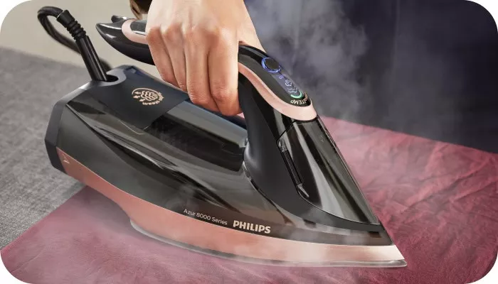 Osoba prasuje tkaninę żelazkiem z napisem \'Azur 8000 Series PHILIPS\'. Żelazko emituje parę podczas prasowania.