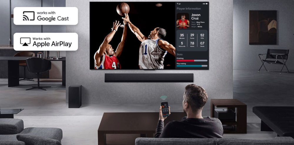 Osoba siedzi na kanapie w salonie, oglądając mecz koszykówki na dużym telewizorze zamontowanym na ścianie. Obok telewizora widoczne są ikony \'works with Google Cast\' i \'works with Apple AirPlay\'.