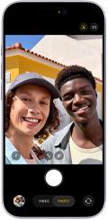 Smartfon z widocznym ekranem aplikacji aparatu fotograficznego. Na ekranie widoczny jest przycisk do robienia zdjęć oraz opcje \'VIDEO\' i \'PHOTO\'.