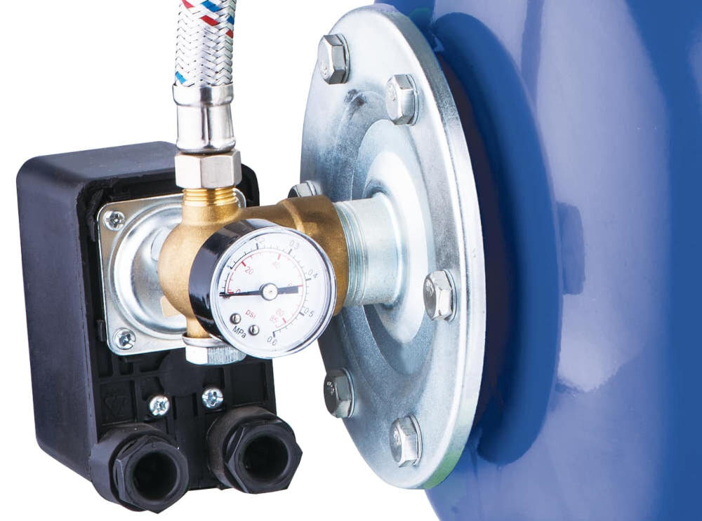 Obraz przedstawia zbliżenie na element hydroforu z manometrem i metalowym złączem. Widoczna jest także część niebieskiego zbiornika oraz czarny element z dwoma złączami.