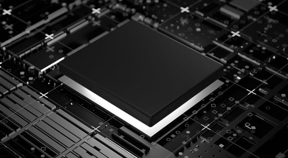 Obraz przedstawia czarny kwadratowy element elektroniczny umieszczony na ciemnej, geometrycznej powierzchni z wzorami w kształcie krzyżyków i prostokątów. Element jest podświetlony od spodu białym światłem.