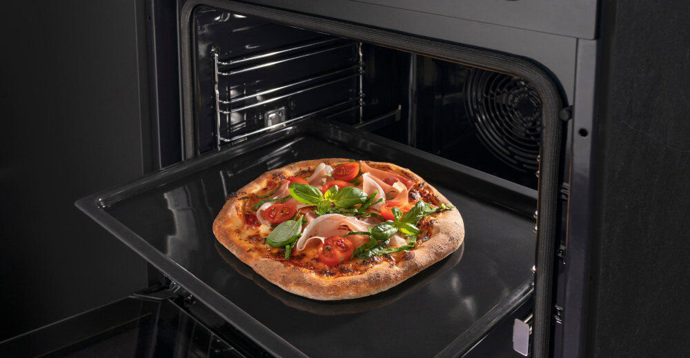 Otwarty piekarnik z widoczną pizzą na blasze. Wnętrze piekarnika jest czarne i ma metalowe prowadnice.