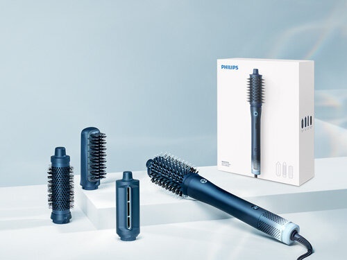 Na obrazie widoczna jest suszarko-lokówka z kilkoma wymiennymi końcówkami oraz pudełko z logo PHILIPS. Produkt jest w kolorze ciemnoniebieskim i znajduje się na jasnym tle.