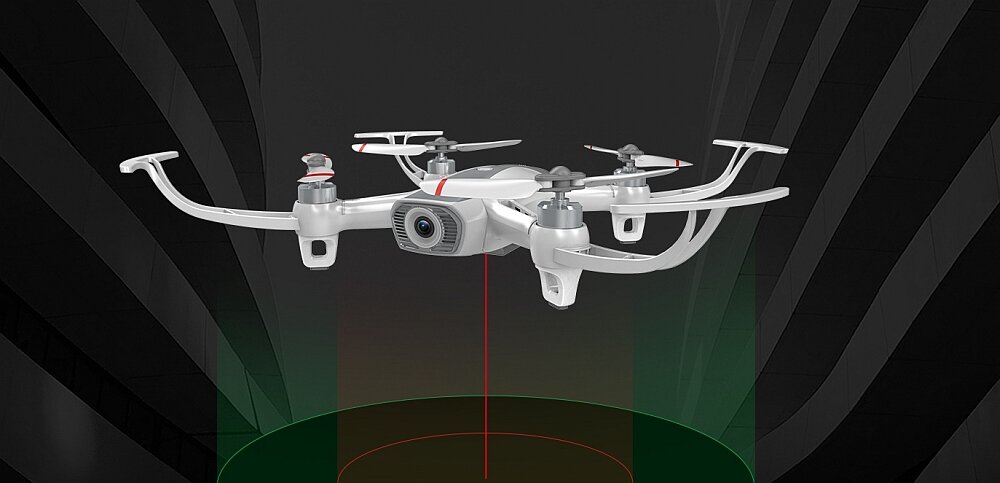 Na obrazie widoczny jest biały dron z kamerą, unoszący się w powietrzu na tle ciemnego, futurystycznego tła. Dron ma cztery śmigła i emituje czerwony promień w dół.