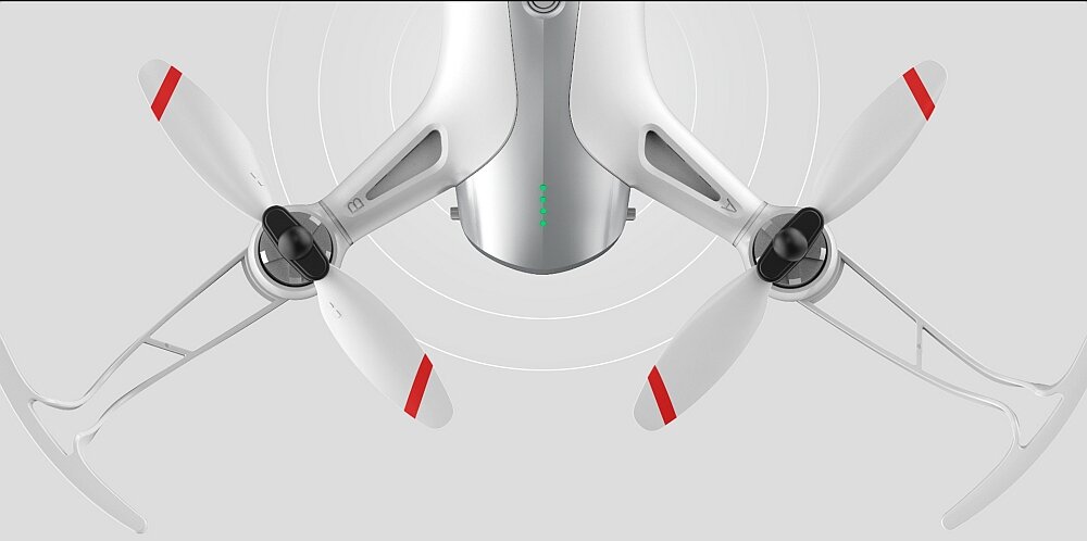 Obraz przedstawia biały dron z czterema śmigłami, z czerwonymi oznaczeniami na końcach. Na korpusie widoczne jest logo \'SYMA\'.