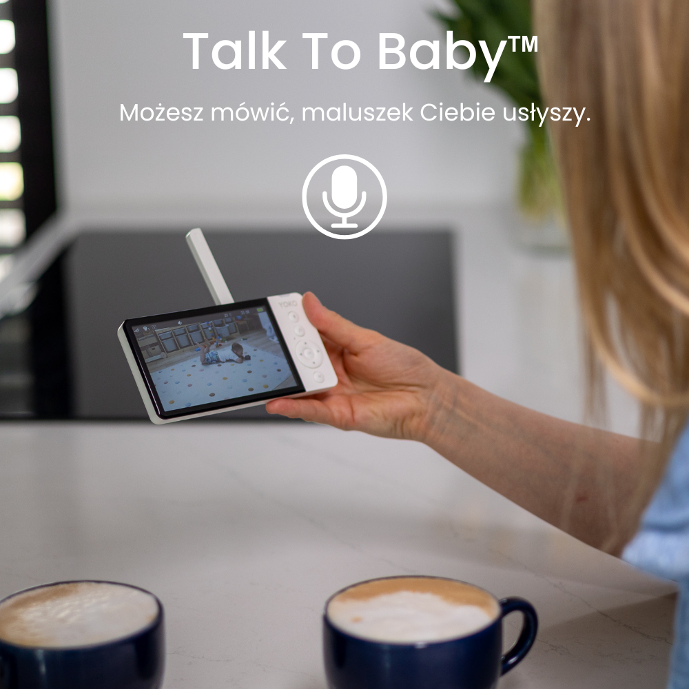 Osoba trzyma urządzenie z ekranem, na którym widać dziecko na macie. Na obrazie znajduje się tekst: \'Talk To Baby™ Możesz mówić, maluszek Ciebie usłyszy.\'