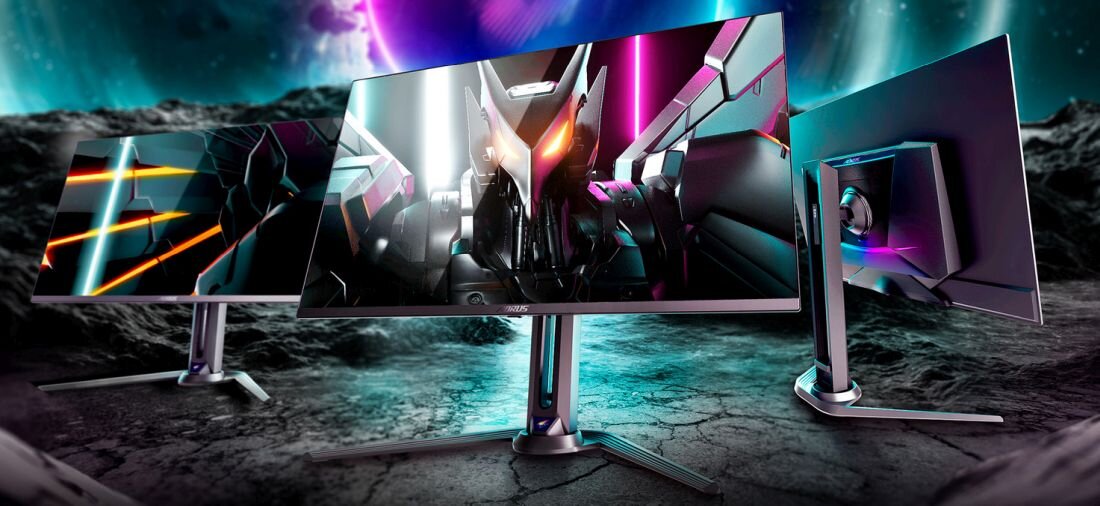 Trzy monitory z futurystycznymi grafikami na ekranach, ustawione na tle kosmicznego krajobrazu. Logo \'AORUS\' widoczne na dolnej ramce środkowego monitora.