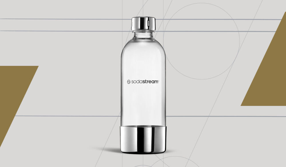 Przezroczysta butelka z metalowym korkiem i podstawą, z logo \'sodastream\' na środku. Tło jest szare z geometrycznymi wzorami i złotymi trójkątami.