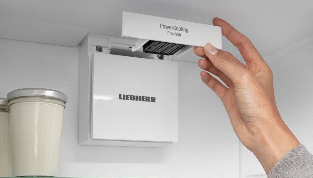 Wnętrze lodówki z widocznym systemem PowerCooling FreshAir. Na urządzeniu widnieje logo LIEBHERR, a obok znajdują się dwa pojemniki z metalowymi pokrywkami.
