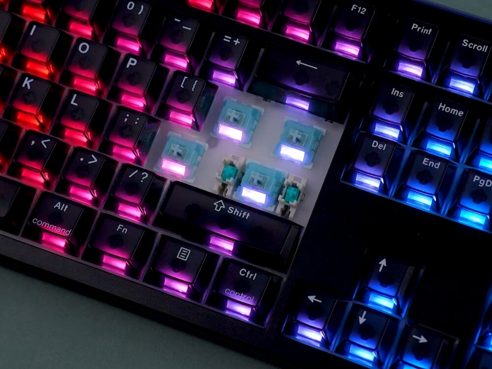 Klawiatura mechaniczna z podświetleniem RGB, z widocznymi klawiszami i przełącznikami. Klawisze mają różne kolory podświetlenia, w tym różowy, niebieski i fioletowy.