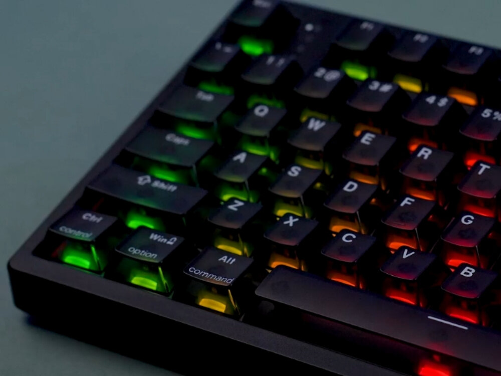 Czarna klawiatura z podświetleniem RGB, na której widoczne są klawisze z literami i symbolami. Klawisze mają różne kolory podświetlenia, w tym zielony, żółty i czerwony.