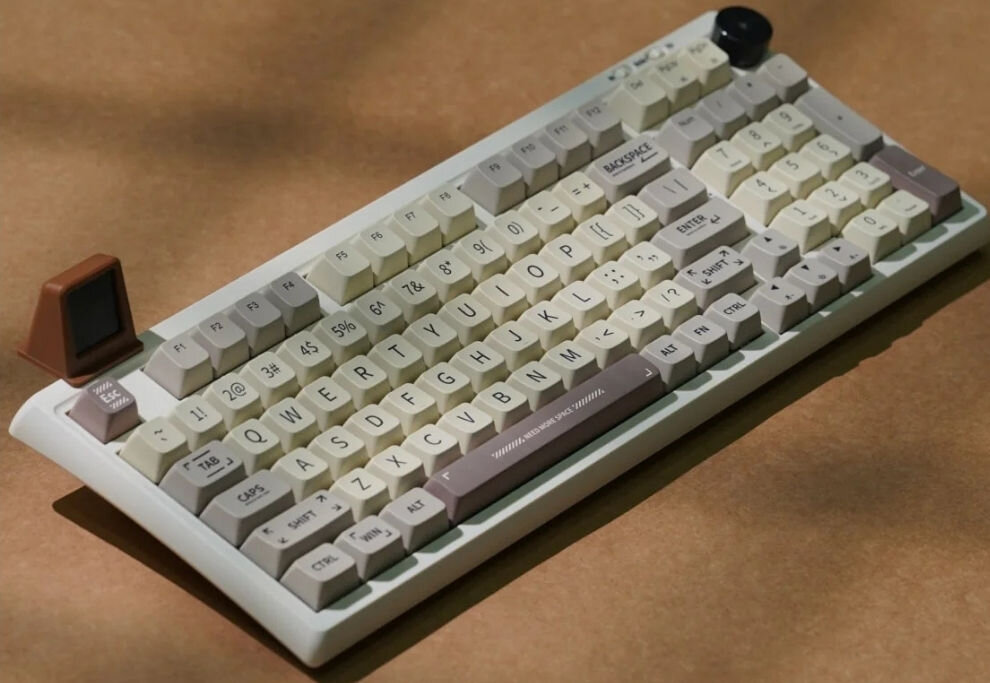 Klawiatura mechaniczna w stylu retro z klawiszami w odcieniach bieli i szarości oraz brązowym elementem dekoracyjnym. Widoczny napis na klawiszu: \'BACKSPACE\'.