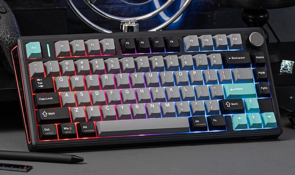 Klawiatura mechaniczna z podświetleniem RGB, posiada klawisze w kolorach czarnym, szarym i turkusowym. Widoczne są klawisze funkcyjne, literowe oraz numeryczne, a także pokrętło w prawym górnym rogu.